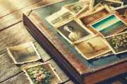 DALL·E 2024 06 16 14.04.49 An old photo album lying on a wooden table, with a mix of yellowed and colorful photos sticking out slightly. The scene is bathed in soft sunlight, cr