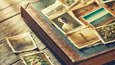DALL·E 2024 06 16 14.04.49 An old photo album lying on a wooden table, with a mix of yellowed and colorful photos sticking out slightly. The scene is bathed in soft sunlight, cr